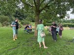 Menschen stehen im Schatten eine Baumes auf einer Wiese und reden miteinander