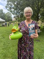 Eine Frau hält eine große grüne Plastikente udn ein Buch in den Händen