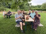 Menschen sitzen auf Bierbänken an einem Tisch auf einer Wiese